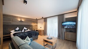 A modern hotel room with a large bed, a sofa, a TV, and a wooden floor. - Hotel Stubai (Schönberg im Stubaital)