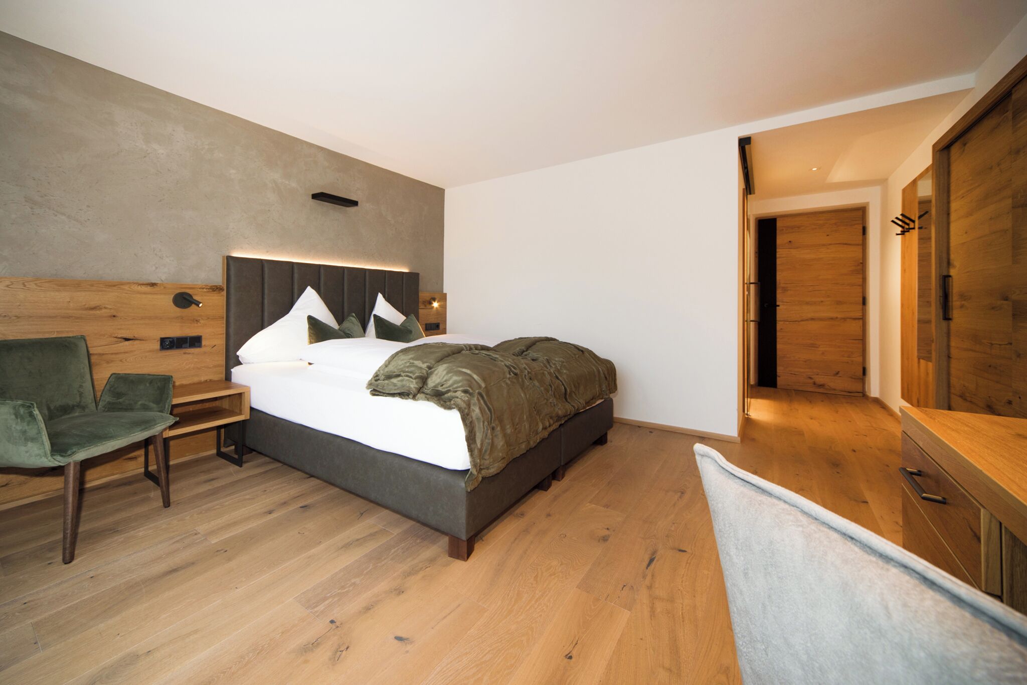Una camera da letto moderna con un letto grande, una testiera in legno, una sedia verde e un armadio in legno.