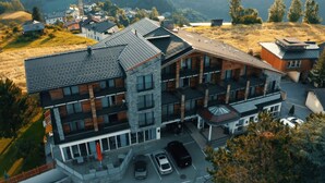 A modern multi-story building with a sloped roof, large windows, and a parking area with several cars. - Hotel Stubai (Schönberg im Stubaital)