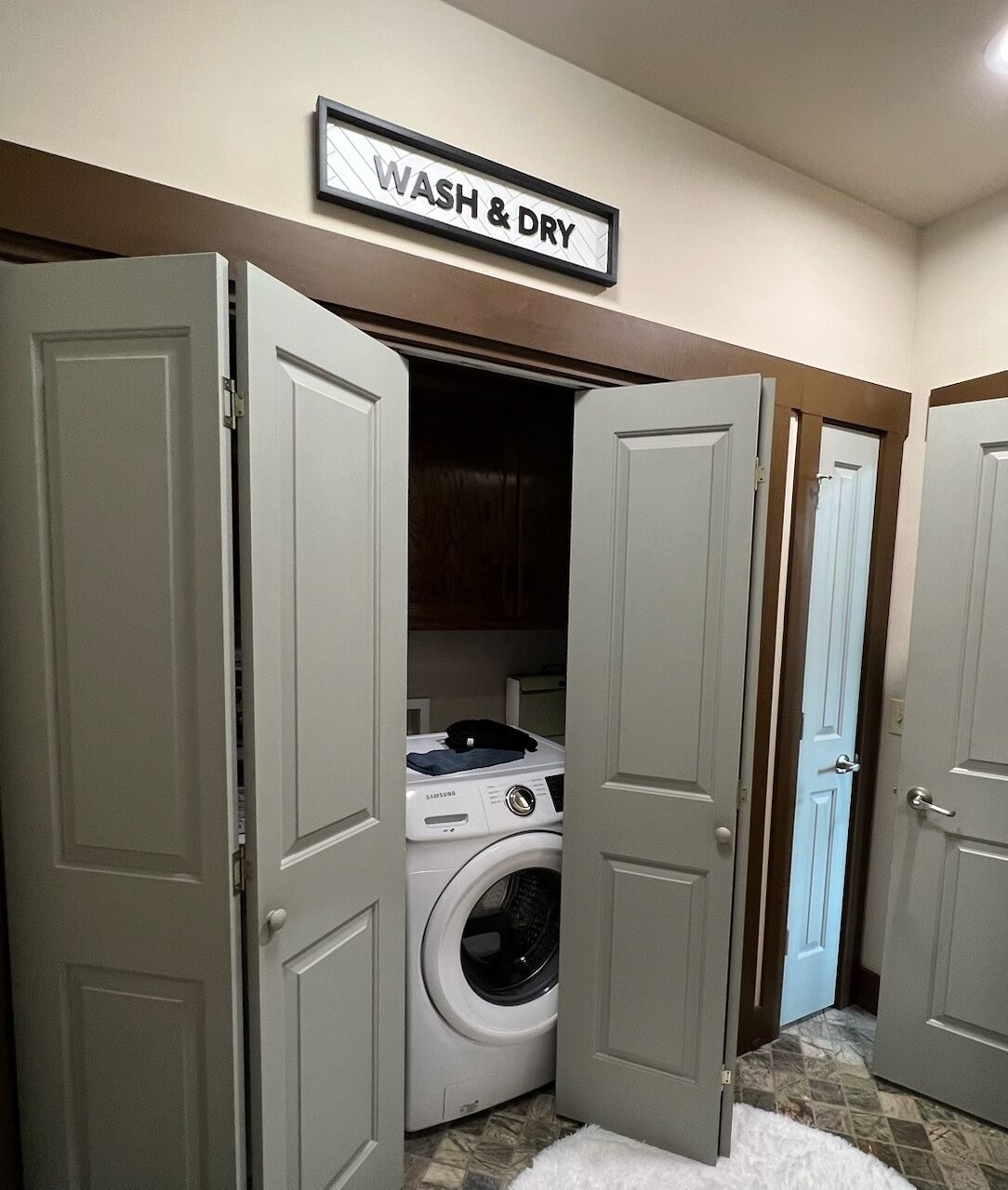 Une buanderie équipée d’un lave-linge, avec deux portes ouvertes et un panneau indiquant « LAVAGE ET SÉCHAGE ».