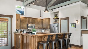 Een keuken met houten kastjes, een centraal eiland met barstoelen, roestvrijstalen apparatuur en hanglampen.