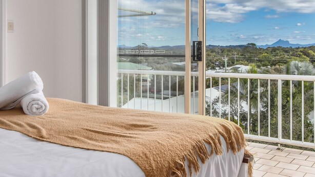 A hotel room with a bed, a large window, and a view of a bridge and mountains.