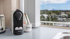 A kitchen with a coffee maker, a Breville coffee grinder, and a coffee pod holder with the text "espresso yourself" on a balcony overlooking a residential area.