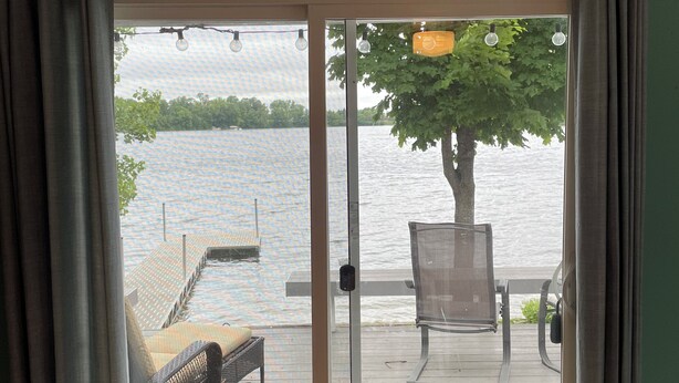 On aperçoit, à travers une porte-fenêtre coulissante, une terrasse en bois avec une chaise et un banc, d’où l’on a vue sur une étendue d’eau.