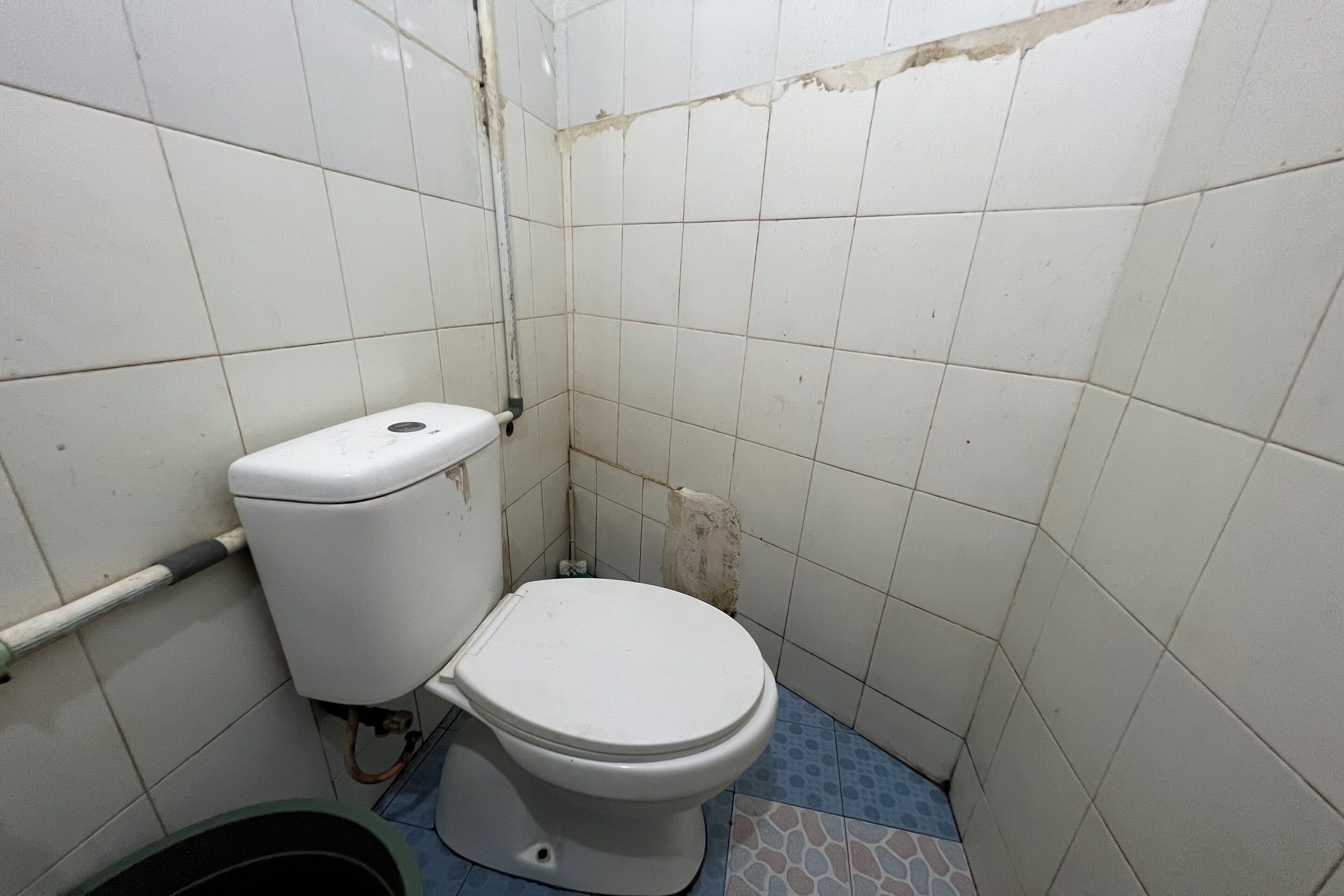 A small, basic bathroom with a toilet, a visible pipe, and a tiled floor.