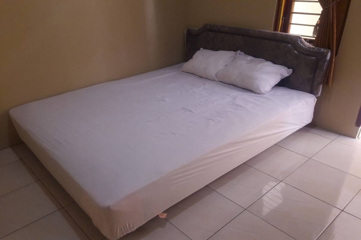 A neatly made bed with white linens in a room with beige walls and tiled flooring.