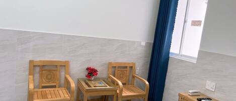 Una habitación pequeña con dos sillas de madera, una mesita y un armario de madera.