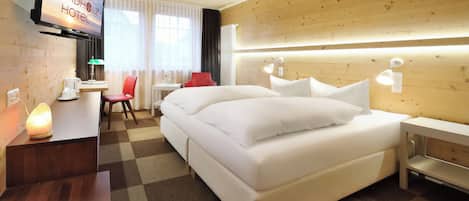 Habitación de hotel con cama, mesitas de noche, escritorio con lámpara, televisión y ventana con cortinas.