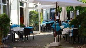 An outdoor dining area with tables and chairs, covered by umbrellas, and a glass door entrance. - Hotel Müller Café & Wein . Mondholzhotel (Veitshoechheim)