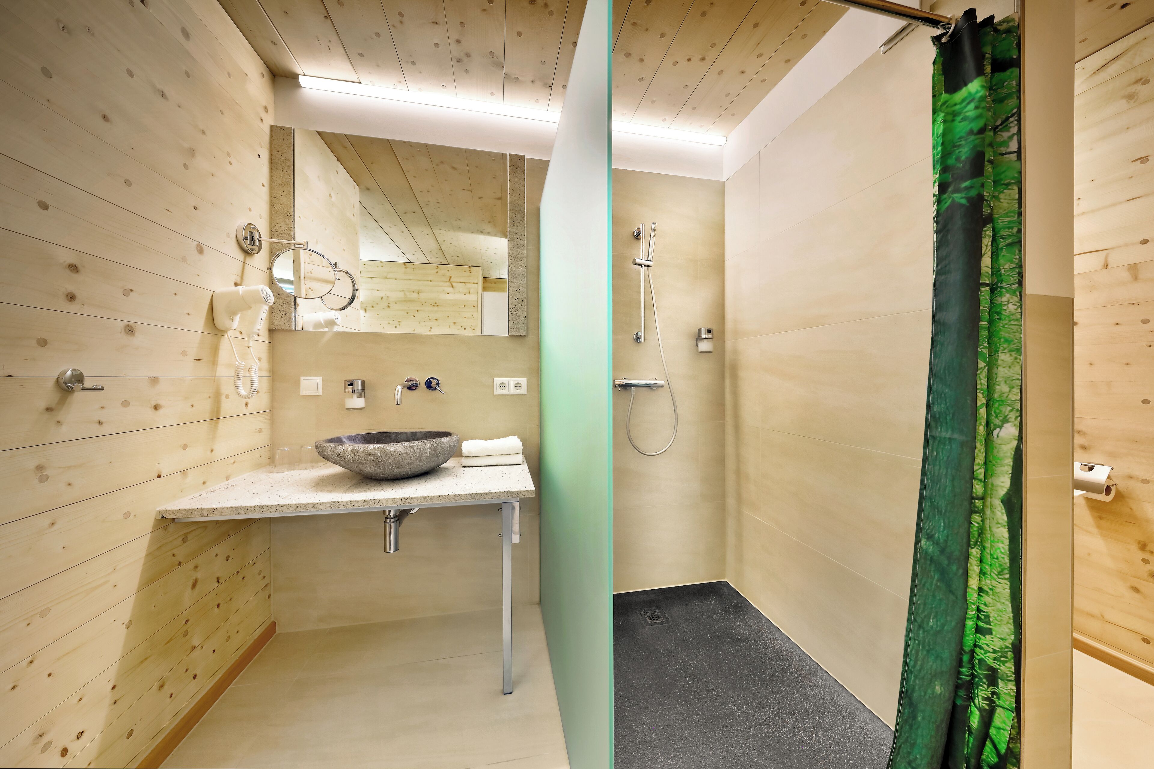 A modern bathroom with a wooden wall, a sink with a bowl, a mirror, a hairdryer, and a shower with a green curtain.