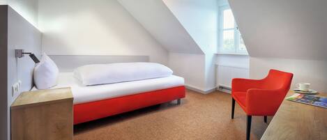 Una habitación moderna con una cama, una silla roja, una mesita de madera y una ventana.