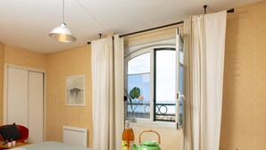A hotel room with a bed, a dining table with breakfast items, a window with curtains, and a view of the sea.