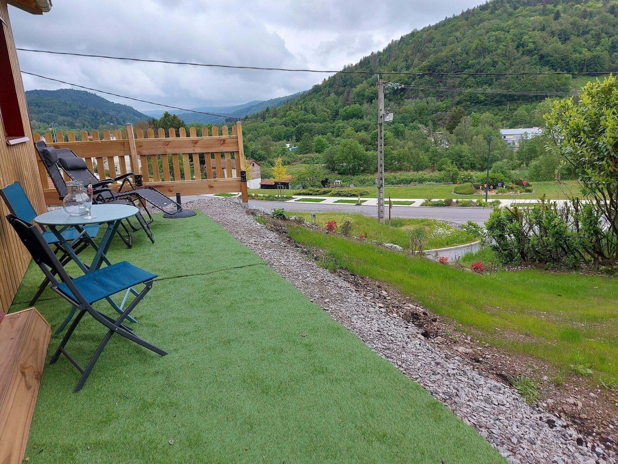 A patio with outdoor furniture, a wooden fence, and a view of a road and greenery.