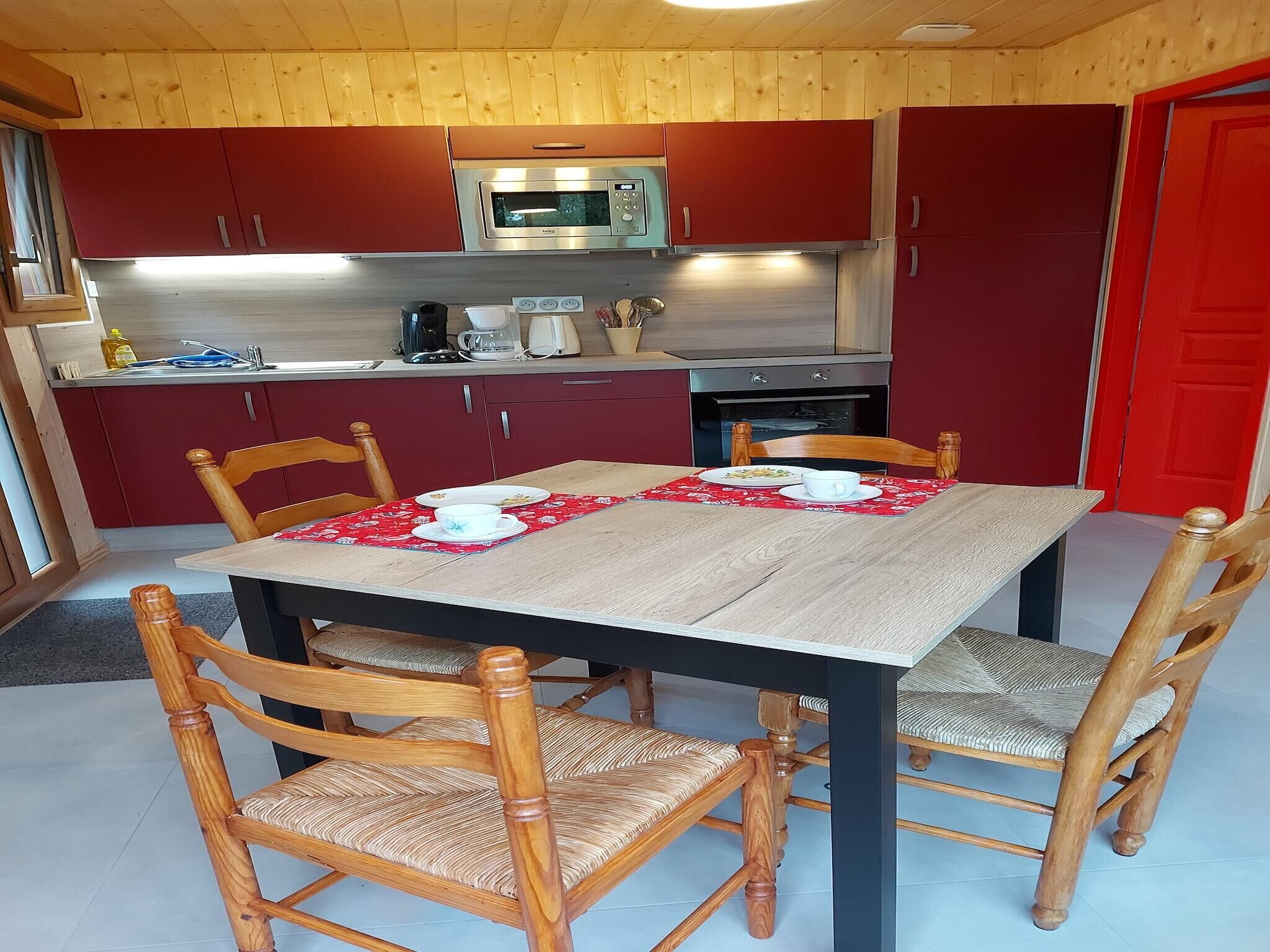 Una cocina compacta con armarios rojos, microondas y estufa. Hay una mesa de comedor con sillas y un mantel individual rojo.