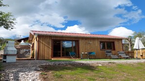 A wooden cabin with a red roof, large sliding glass doors, and a patio area with outdoor seating.