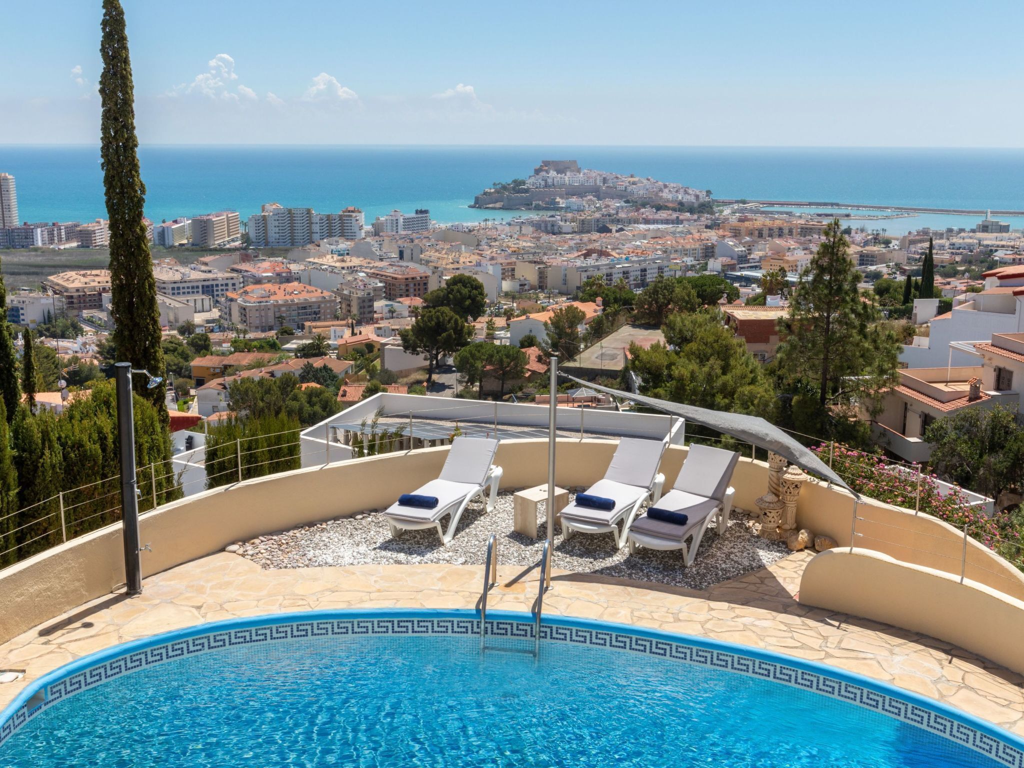 Une piscine sur le toit, agrémentée de chaises longues, offrant une vue dégagée sur le paysage urbain et la mer, et un bâtiment remarquable à l’horizon.