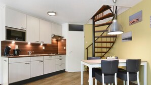 A modern kitchen with white cabinets, a wooden countertop, and a built-in microwave. There is a dining area with a white table and black chairs. A spiral staircase with a wooden railing leads to another level. - Holiday Home by Grevelingenmeer & Brouwersdam (Brouwershaven)