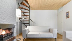 A modern living room with a fireplace, white sofa, and a wooden staircase. - Holiday Home near Grevelingenmeer Lake (Brouwershaven)