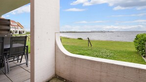 A patio with a view of the sea, a grassy area, and a building in the background.