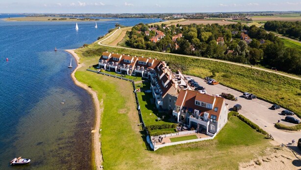 An aerial view of a coastal hotel with multiple buildings, a marina, and a road leading to the property.