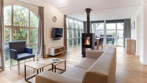 A spacious living room with a large window, a fireplace, a sofa, a TV, and a dining area.