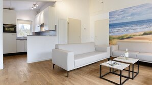 A modern living room with a white sofa, a coffee table, and a painting of a beach scene on the wall.