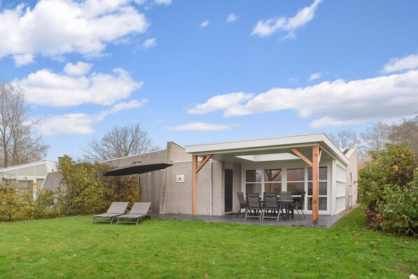 Une maison moderne dotée d’un patio couvert, d’une pelouse et d’un coin repas avec des chaises et une table.