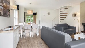 A modern living room with a sofa, dining table, and chairs. There is a staircase leading to another level.