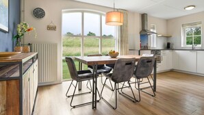 A modern kitchen with a dining area, large windows, and a view of the outdoors.