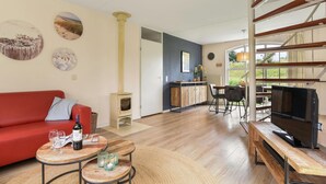 A modern living room with a red sofa, a wooden coffee table with a bottle of wine, and a TV on a wooden stand.