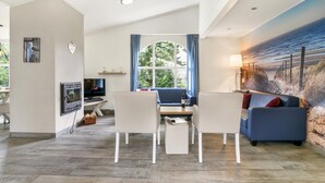 Een moderne woonkamer met een eethoek, een flatscreen-tv, een open haard en een groot raam met gordijnen.