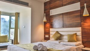 A modern hotel room with a large bed, wooden headboard, two bedside lamps, and a window with curtains. - HOTEL SUN 'N' SHINE (Bhavnagar)