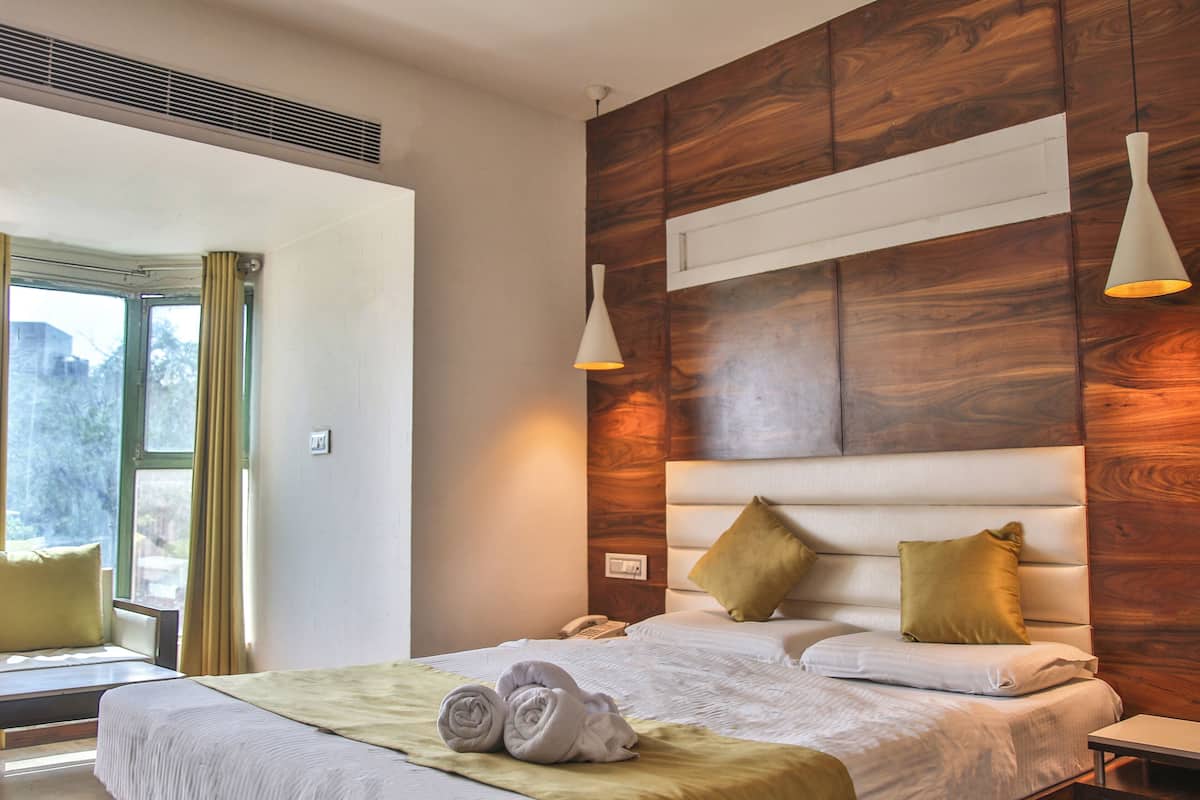 A modern hotel room with a large bed, wooden headboard, two bedside lamps, and a window with curtains.