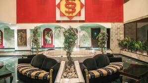 A lobby with a central fountain, seating areas, and a large wall with a dollar sign symbol. - HOTEL SUN 'N' SHINE (Bhavnagar)
