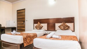 A hotel room with two beds, each with a wooden headboard and patterned bedspreads. There is a small bedside table with a telephone and a towel on each bed. - HOTEL SUN 'N' SHINE (Bhavnagar)