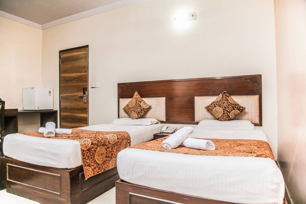 A hotel room with two beds, each with a wooden headboard and patterned bedspreads. There is a small bedside table with a telephone and a towel on each bed.