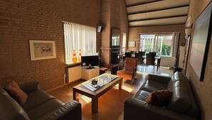 Een ruime woonkamer met een bakstenen muur, een open haard, een televisie en een eethoek met stoelen en een tafel.