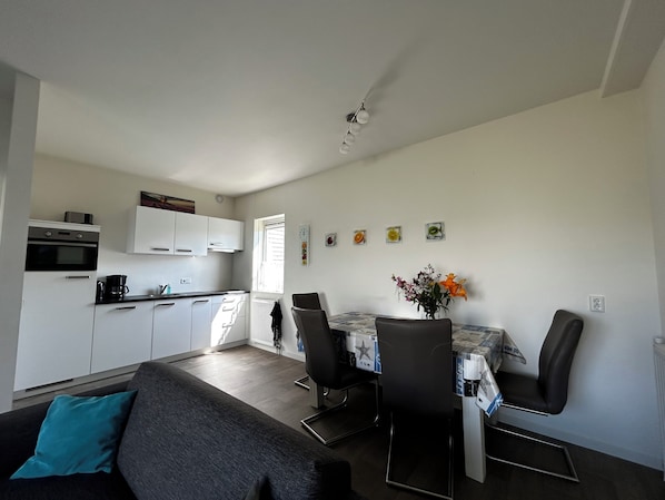 A compact living space with a kitchenette, a dining area with a table and chairs, and a sofa with a teal pillow.