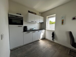 A compact kitchen with white cabinets, a black countertop, and a window with a view of greenery.