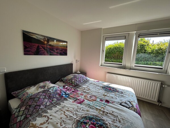 A bedroom with a bed, a window with a view of greenery, a radiator, and a wall-mounted picture. - 2 bedroom accommodation in Julianadorp aan Zee (Julianadorp aan Zee)