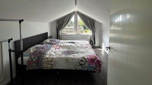 Ein Schlafzimmer mit Bett, einem Fenster mit Vorhängen, einem Heizkörper und einer Deckenleuchte.