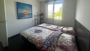 A bedroom with two beds, a painting, a window, and a radiator.