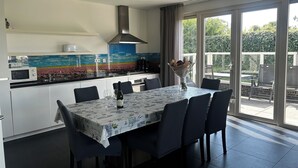 A modern kitchen with a dining area, a large window, and a view of greenery outside.