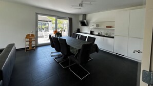 Une cuisine moderne avec un coin repas, comprenant une grande table, des chaises et une vue à travers la porte vitrée.