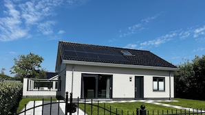 Une maison moderne dotée d’un toit recouvert de panneaux solaires, d’une allée fermée par un portail et d’une pelouse bien entretenue.