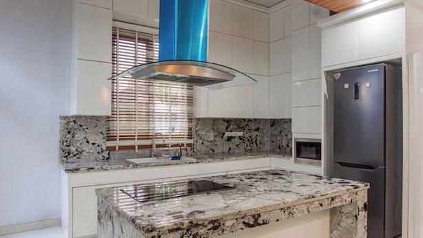 Una cocina moderna con encimera de granito, electrodomésticos de acero inoxidable y un respiradero azul en el techo.
