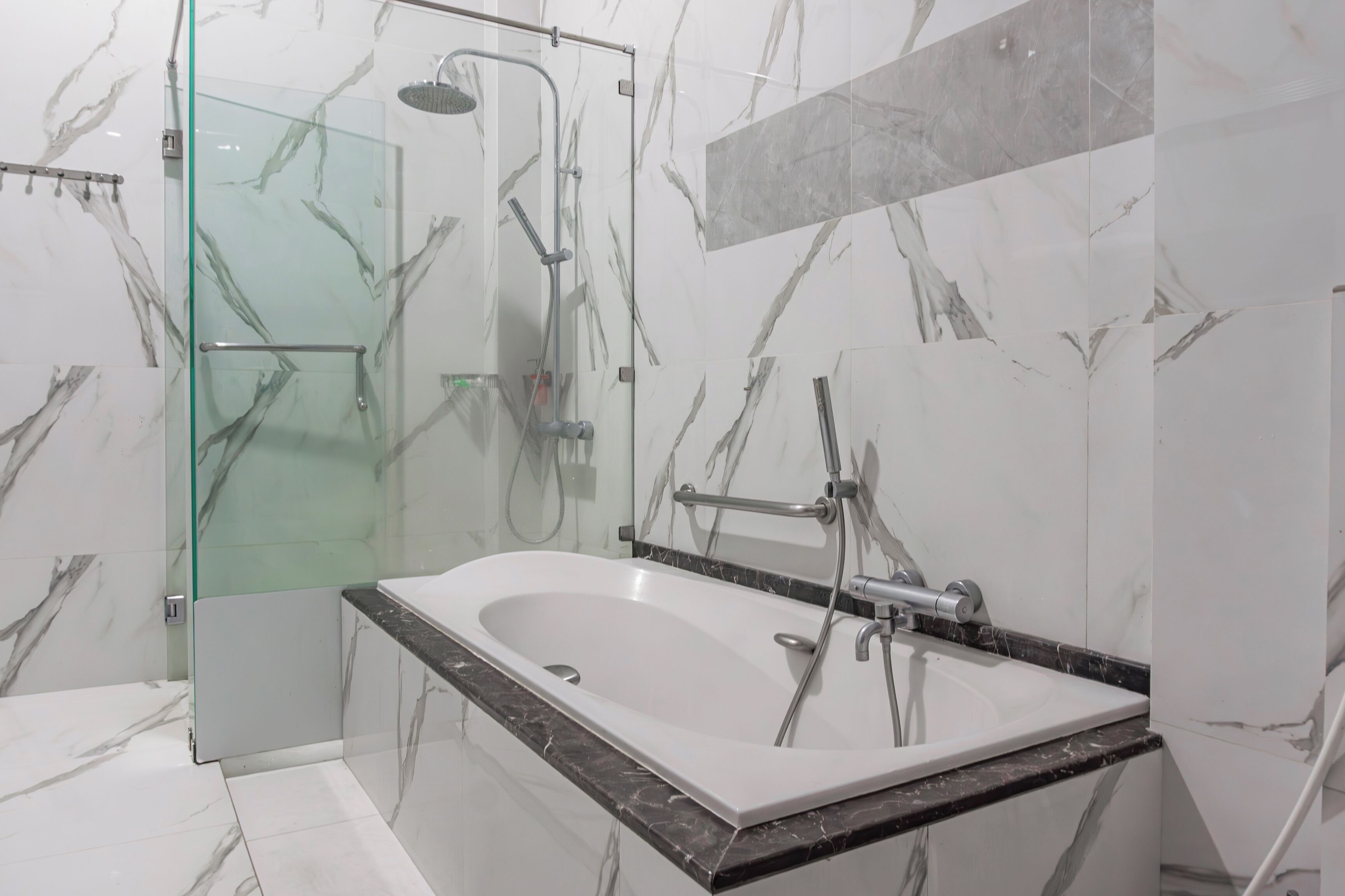 A modern bathroom with a glass-enclosed shower, a freestanding bathtub, and marble-patterned walls.