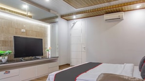 Un dormitorio moderno con una televisión de pantalla plana, una cama con colcha negra y roja, techo de madera y un equipo de aire acondicionado.
