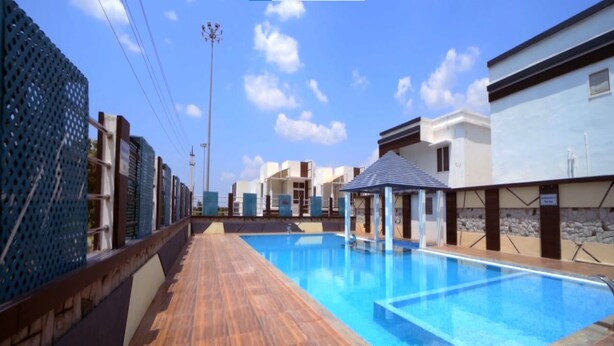 A swimming pool with a wooden deck, surrounded by modern buildings and a clear sky. - Green Royale Resorts (Tarangambadi)