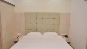 A neatly made bed with a tufted headboard, two bedside tables with a phone and a lamp, and a light-colored wall. - Green Royale Resorts (Tarangambadi)